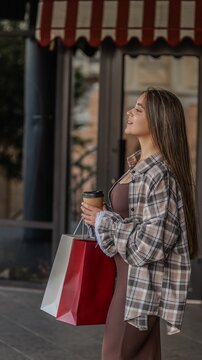 Young woman with long hair holding shopping bags and a coffee cup outside a boutique storefront