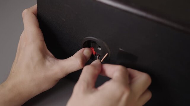 Closeup shot of person connecting positive and negative speaker wires to spring clip terminals on back of home theater, stereo audio speaker. Hifi setup and installation, close-up, slow motion.