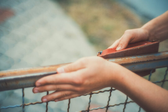 Close-up of hands using a sanding block to smooth a rusty metal fence before painting. Motion blur adds a raw, authentic feel. DIY restoration photo for craft and renovation projects