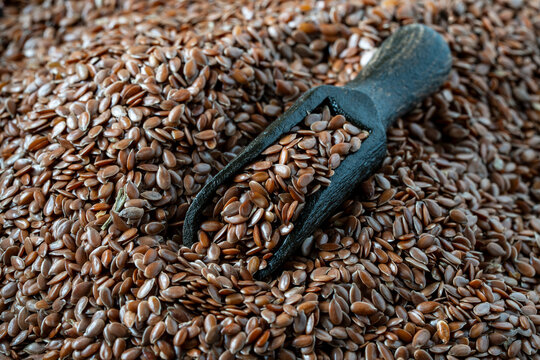 Brown flax seeds heap with wooden scoop. Closeup of organic flaxseeds or linseed pile with dark wood scoop. Healthy superfood ingredient backdrop for vegetarian nutrition, wellness and marketing