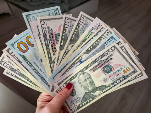 Woman&rsquo;s hand with red manicure holding a fan of US dollar bills, fifty and hundred dollar banknotes in cash, dark wooden background. Money and finance concept, grainy film texture, high quality photo