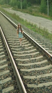 Solitary child navigates quiet expanse of train tracks her movement steady and purposeful. surrounding environment features gravel paths alongside greenery with dirt road running parallel