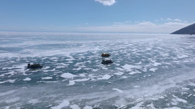 High angle aerial view of hovercraft vehicles moving across the vast frozen ice surface of Lake Baikal in Irkutsk Oblast, Russia during cold sunny winter day with blue sky and snow