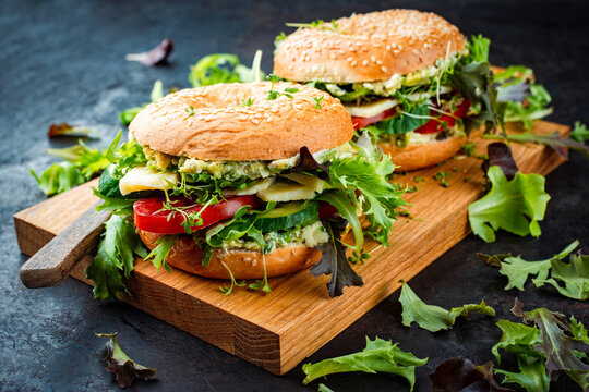 Classic fingerfood fastfood snack -  traditional sesam bagels - bread bun rolls sandwich with avocado guacamole, cheese and vegetable salad served as close-up on a wooden board