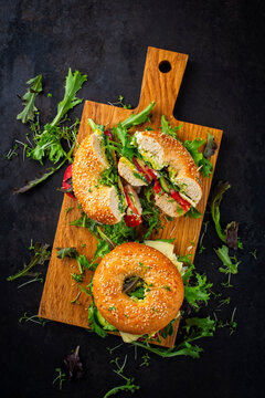 Classic fingerfood fastfood snack -  traditional sesam bagels - bread bun rolls sandwich with avocado guacamole, cheese and vegetable salad served as top view on a wooden board