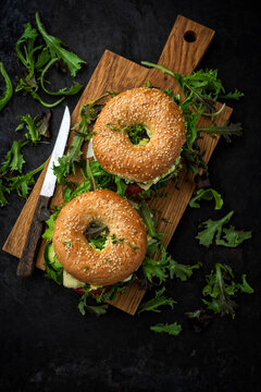 Classic fingerfood fastfood snack -  traditional sesam bagels - bread bun rolls sandwich with avocado guacamole, cheese and vegetable salad served as top view on wooden board