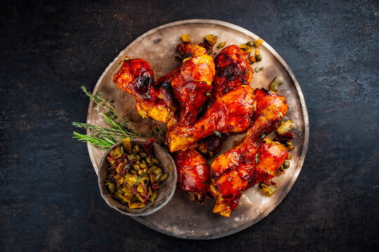 Traditional oven roasted barbecue chicken drumsticks with hot honey chili sauce and gherkin relish served as top view on a rustic design plate