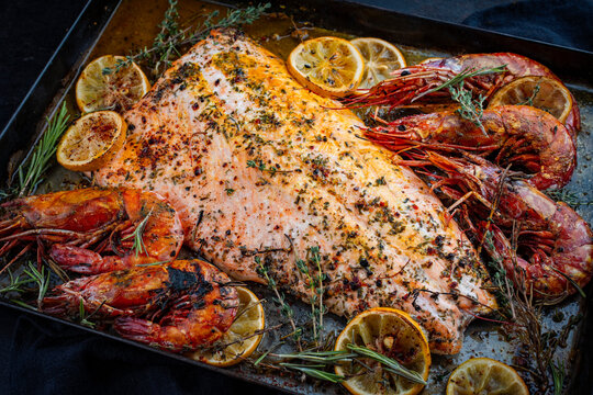 Oven baked salmon filet spicy roast with white tiger prawns, herbs and lemon slices served as close-up on a baking roast tray