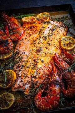 Oven baked salmon filet spicy roast with white tiger prawns, herbs and lemon slices served as close-up on a baking roast tray