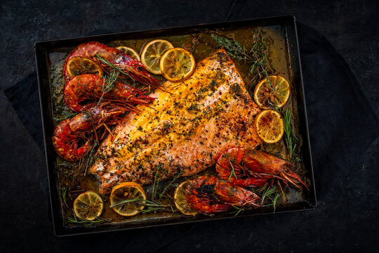 Oven baked salmon filet spicy roast with white tiger prawns, herbs and lemon slices served as top view on a baking roast tray