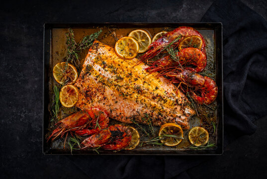 Oven baked salmon filet spicy roast with white tiger prawns, herbs and lemon slices served as top view on a baking roast tray