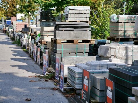 Pallets of stacked concrete paving stones and curb blocks lined up outdoors at building supply depot