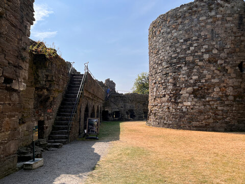 Beaumaris Castle, Isle of Anglesey, - july 17, 2026: A stone staircase with metal handrails rises along a castle wall beside a large round tower, with a dry grass courtyard and gravel path below a cle