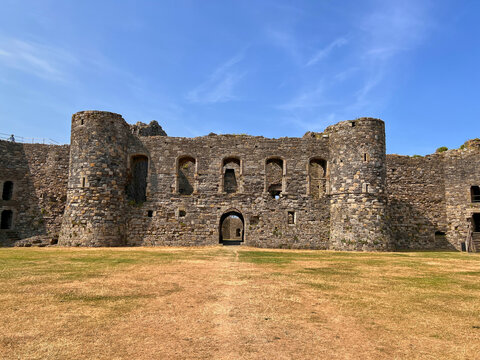 Beaumaris Castle, Isle of Anglesey, - july 17, 2026: The weathered stone inner facade of a medieval castle with two round towers, arched windows and a central archway rises above a dry grass courtyard