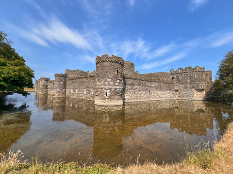 Beaumaris Castle, Isle of Anglesey, - july 17, 2026: A medieval stone castle with round corner towers and crenellated walls stands behind a water-filled moat that reflects the structure under a blue s