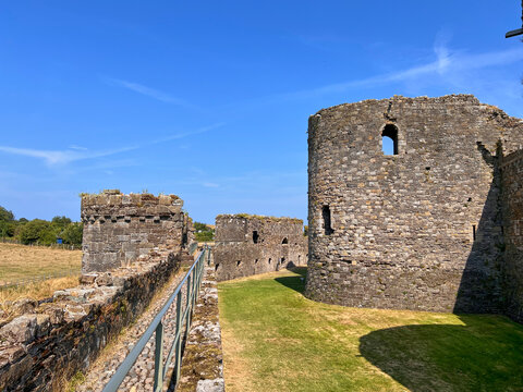 Beaumaris Castle, Isle of Anglesey, - july 17, 2026: Ruined medieval stone castle walls and a round tower stand beside a grass courtyard and a metal handrail under a clear blue sky with thin cloud.