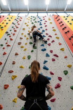 Indoor bouldering gym with climber on wall and instructor spotting
