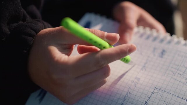 Close up shows two steady hand movements holding bright green pen over graph paper filled with mathematical equations and diagrams. hands wearing dark clothing remain focused on writing