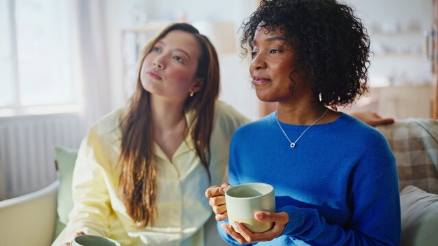 Multiracial women sharing coffee sofa. Two friends talking heartfelt home.