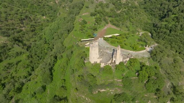 High angle shot of the historic Vatan memorial complex surrounded by lush green mountain slopes in Dagestan, showcasing ancient defensive stone architecture and scenic nature
