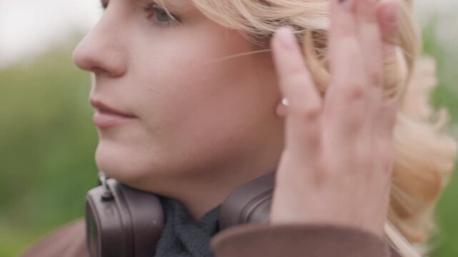 Close up shots show lady with blonde hair as woman adjusts her own hair. brown object resembling audio equipment is near her neck and background remains softly blurred