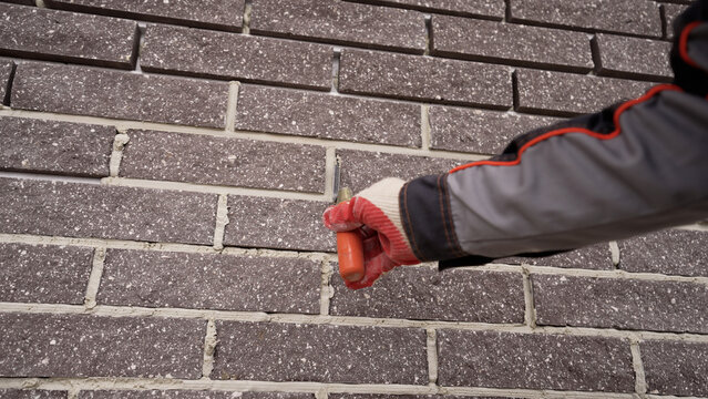Gloved hand with orange pointing trowel smoothing mortar on dark brick wall, building facade restoration and repair