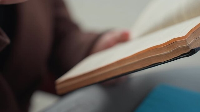 Close up shows someone hand turning pages of open book. white takeaway coffee cup is visible in focus suggesting casual reading environment with soft lighting