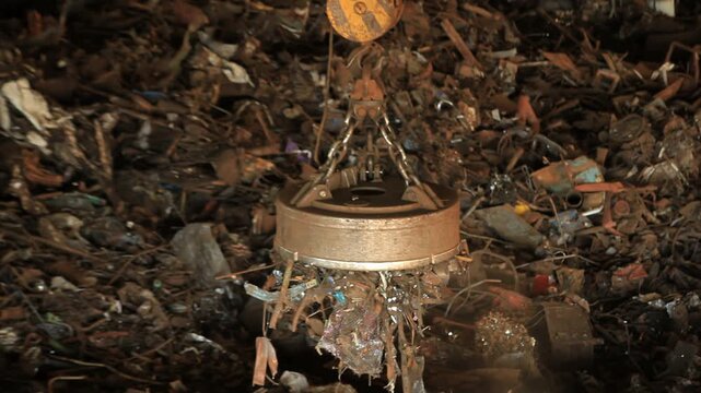 Scrap metal loading electromagnet. Crane dropping iron waste charging bucket.