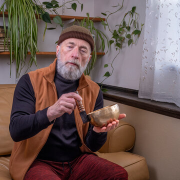 senior man is meditating with a Tibetan singing bowl at home, sound therapy concept