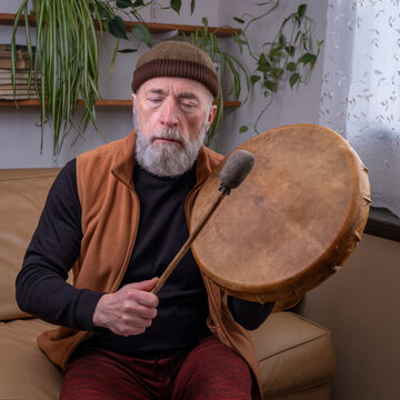 senior man is playing a native American style, shaman drum with a beater at home, lifestyle and hobby concept