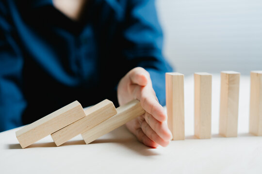 Hand stops falling wooden block representing risk management for calm focus and stability at work with strategic professional planning