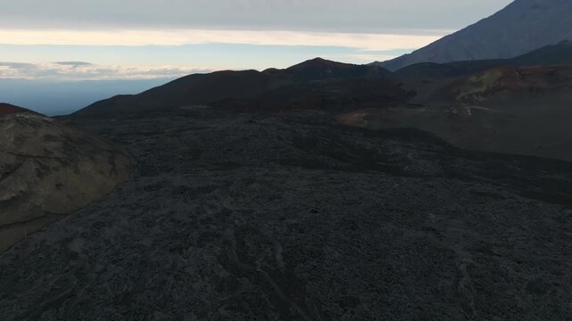 Dramatic aerial footage shows vast fields of solidified dark lava and volcanic cones across the remote volcanic landscape of Tolbachik Dale in Kamchatka Krai, Russia during dusk