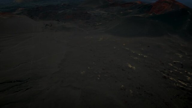 High angle aerial footage capturing the surreal volcanic landscape of cinder cones, slag fields, and dark terrain in the Kamchatka Krai region of Russia during a hazy afternoon