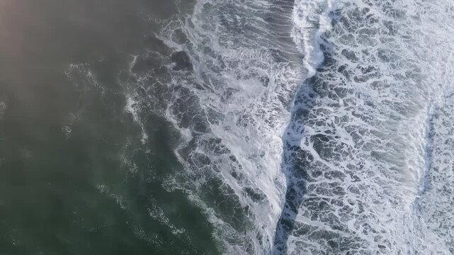Overhead drone footage captures rolling ocean waves breaking into white sea foam near Khalaktyrsky Beach in Kamchatka Krai, Russia, showing dynamic natural water movement and surf texture