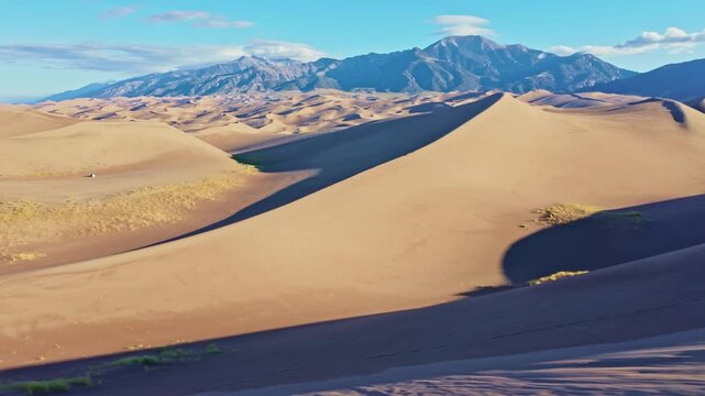 Expansive sand dunes stretch toward distant mountain peaks under clear morning skies in Great Sand Dunes National Park