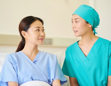 Japanese female doctor in a surgical cap explaining to a young woman patient in a hospital gown before surgery