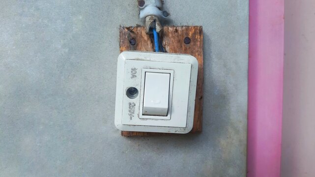 Old electrical light switch mounted on a wooden board on a concrete wall