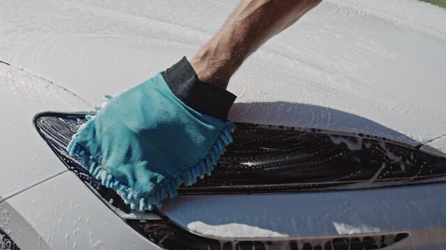 Carwash station. Washing car in workshop. Professional work. Car washer doing manual foam washing in auto detailing service. Polishing car body using microfiber cloth. Car in washing process