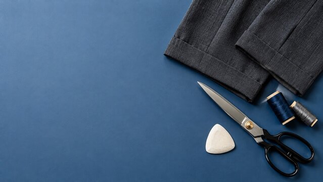 Tailor shears thread and trouser hems on blue background with copy space