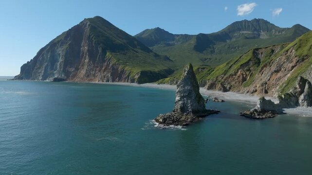 Drone footage shows majestic sea stack and rugged volcanic cliffs along the scenic Pacific Ocean shoreline of Kamchatka Krai in Russia with clear blue water and wild nature