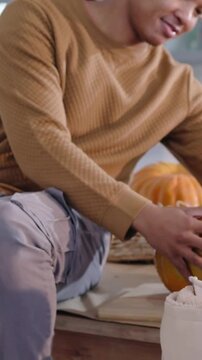 Vertical video: Inspecting pumpkin on workboard dad steadying and carving at kitchen showing child