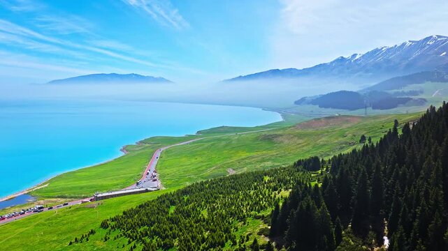 Aerial view of the azure alpine shoreline of Sayram Lake with green meadows and forests in Xinjiang, China