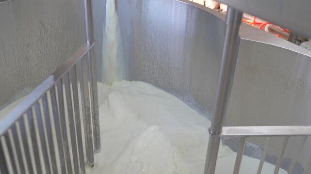 Industrial cheesemaking process with milk pouring and mixing in a large metal tank at the factory