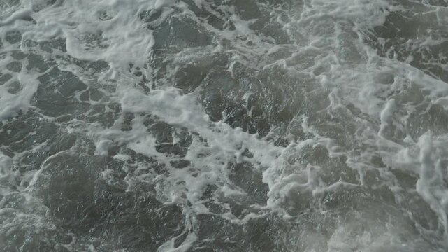 Top down view of agitated sea water with white foam swirling around dark rocks