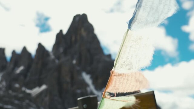 Close up of a faded and frayed fabric flag on a wooden pole in the foreground with jagged Dolomite peaks and a cloudy sky in the background on the Tre Cime di Lavaredo loop in Italy