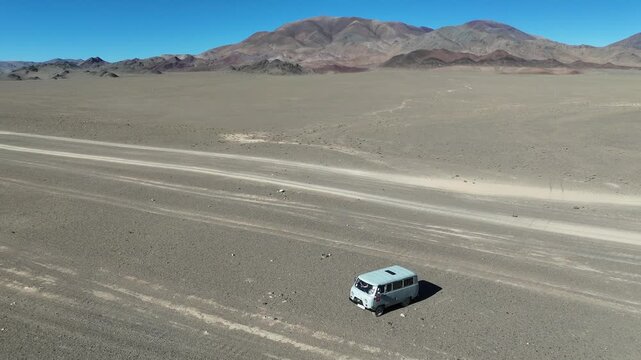 drone shot capturing a classic off-road van driving along a wide dirt track through the arid, expansive desert landscape of the Altai Mountains in Mongolia