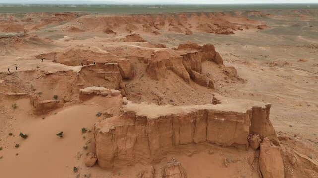 drone footage capturing the iconic red sandstone cliffs, deep ravines, and eroded geological formations of the Flaming Cliffs in the Gobi Desert, Mongolia