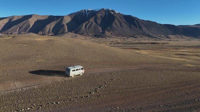 drone shot following a classic overland van driving across an expansive, dusty plateau surrounded by the remote peaks of the Altai Mountains in Mongolia