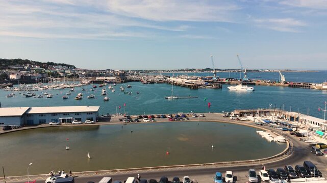 St Peter Port Harbour,Guernsey,Channel Islands.Drone footage over model yacht pond with model boats past,docks to ferry berth and Cambridge Berth to own backdrop with ferry arriving in bright sunshine