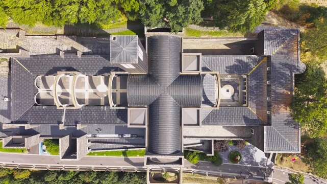 Top-down view of Sanctuary Basilica of Our Lady of Meritxell in Andorra, revealing a cross-shaped roof with curved vaults, stone walls, and surrounding trees